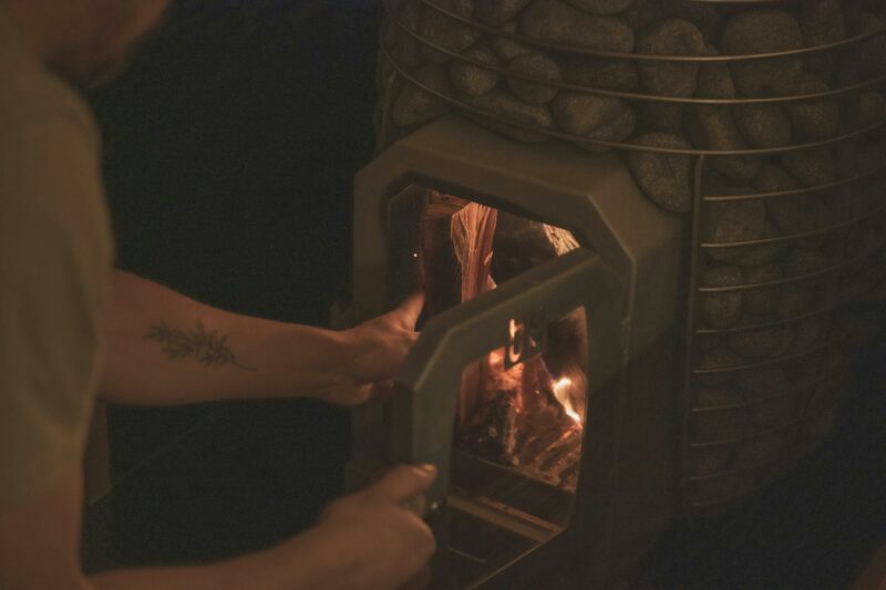 Loading wood into a wood fired Huum sauna heater in dim lighting