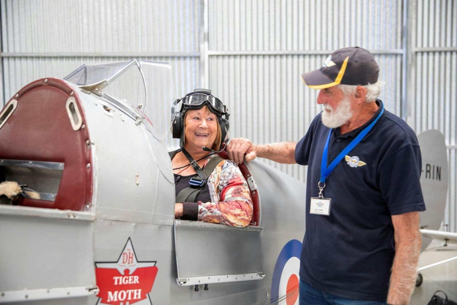 Woman sitting in an old airplane with a flying cap talking to a man standing beside the plane