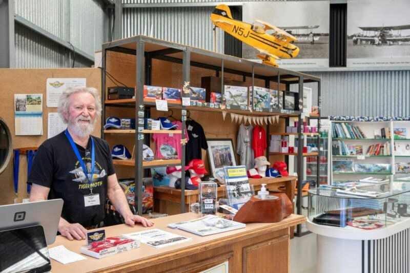 Man standing at a desk with a shelf of merchandise behind him