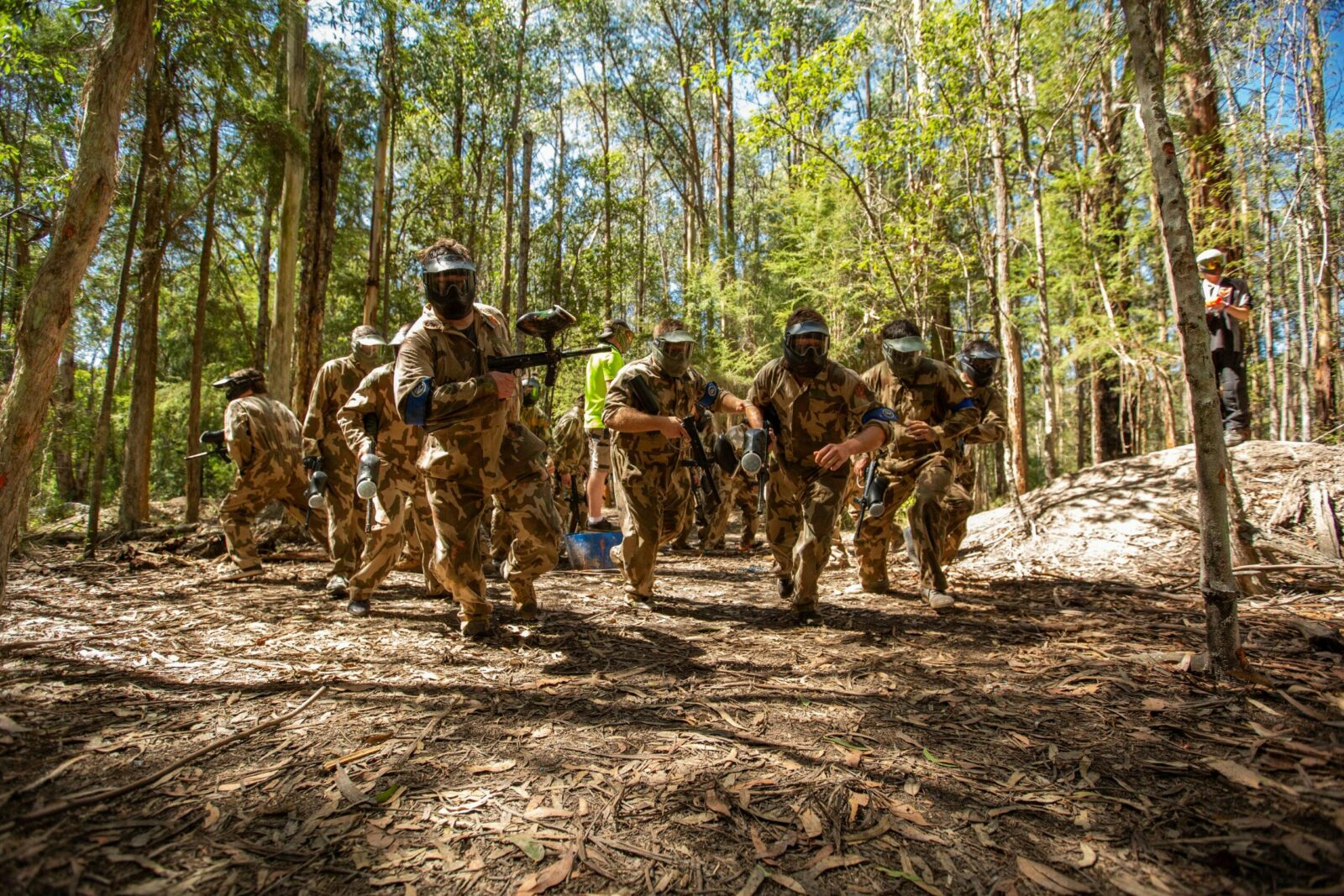 A group in camo gear rushes forward playing paintball in the bush