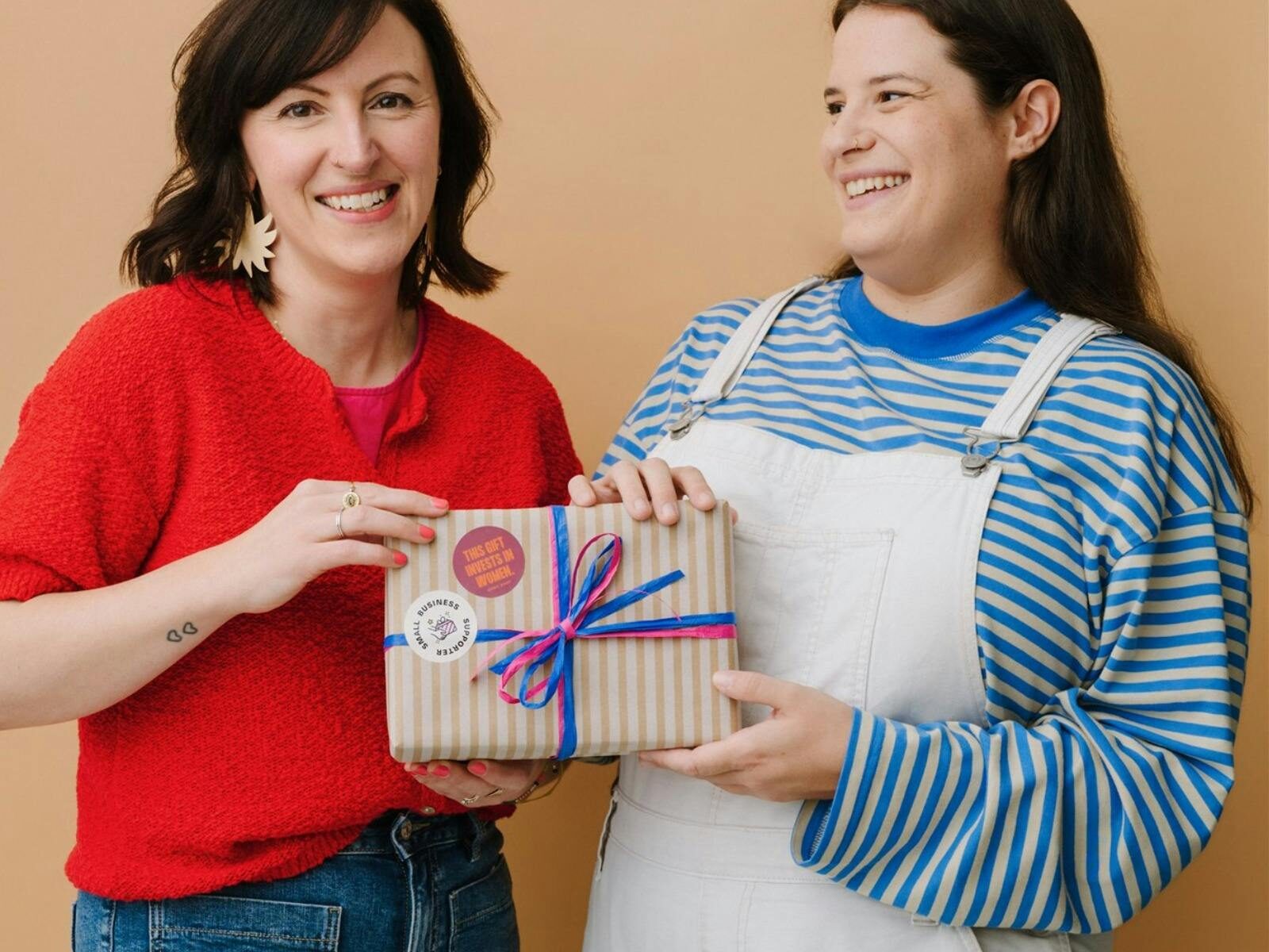 2 women holding gift box that says this gift invests in women