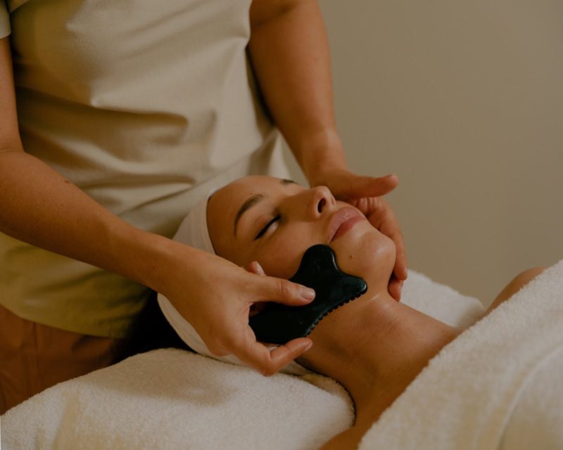 A therapist massaging the guestâs face with a guasha stone