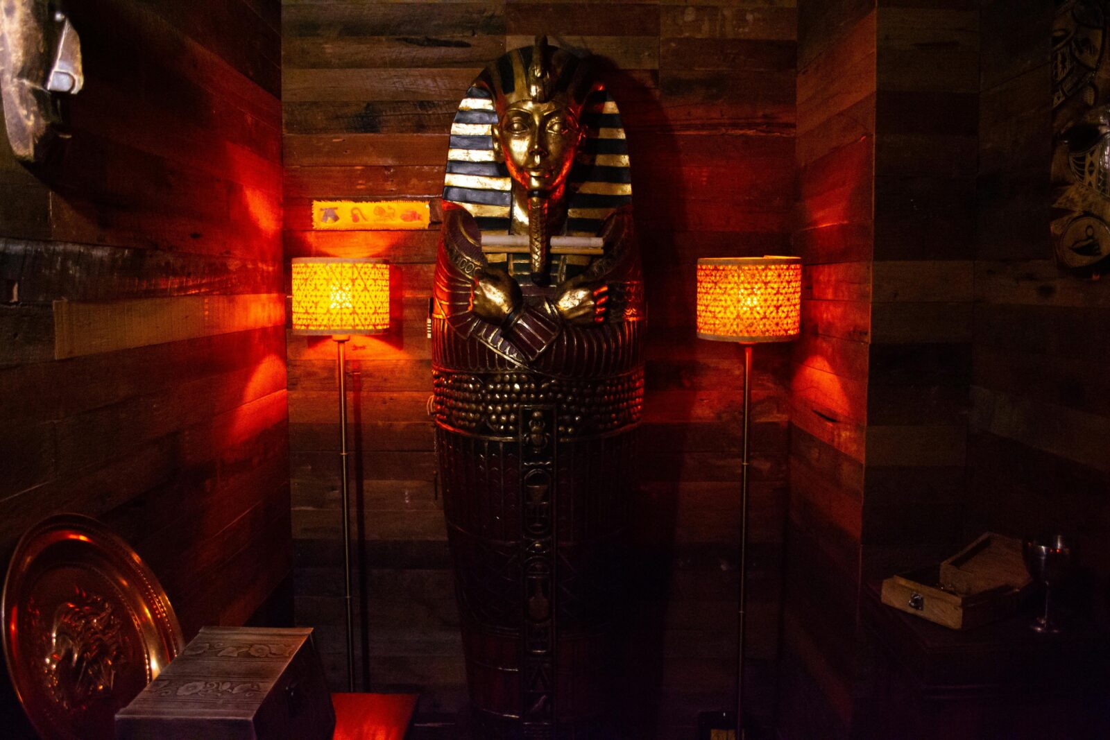 A gold and blue sarcophagus inbetween two glowing orange lamps with a wooden wall behind.