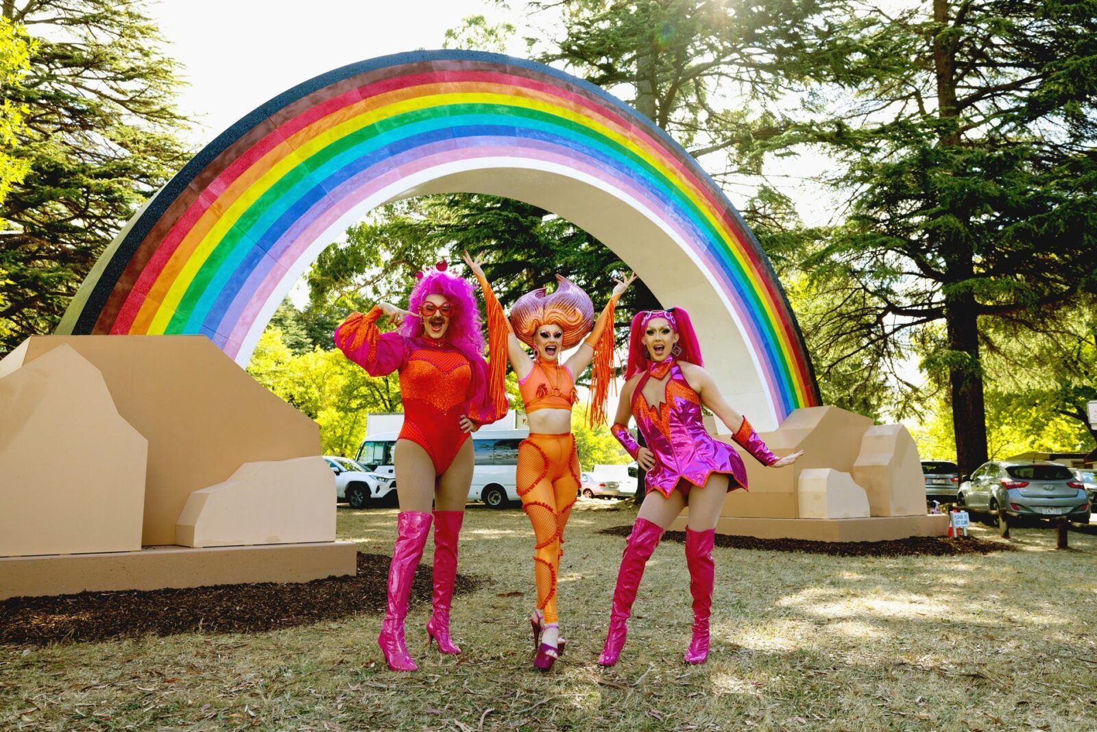 Three drag queens in front of a big rainbow