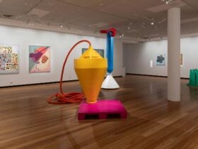 Shot of gallery space with bright sculptures and paintings on wall.