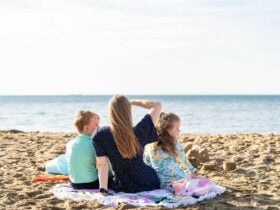 an adult and two children sitting on a towel on the sand looking out to the water