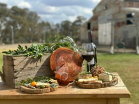 Fresh produce served on timber boards with a bottle of red wine from local wineries on rustic table