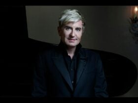Waist-up image of Jean-Yves Thibaudet against a dark background, wearing a black jacket and shirt