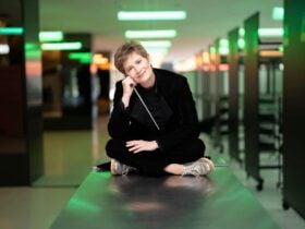 Conductor Anja Bihlmaier sitting with her legs crossed holding a baton.