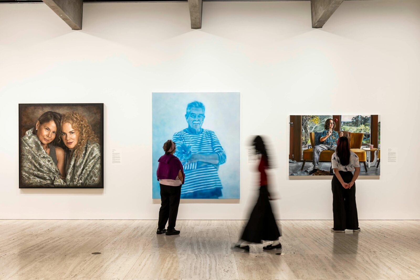 Two women view three portraits hanging on a gallery wall