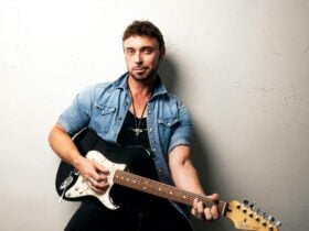 Nathan Foley posing with guitar, in front of white background.
