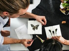 Two people at work bench pinning butterflies on paper