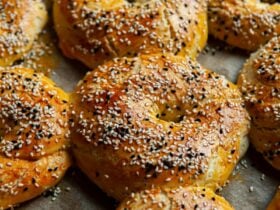 Tray of bagels, freshly baked to golden brown, sprinkled with seeds.