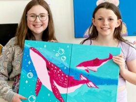 Friends showing a canvas painting of whales that they have painted together