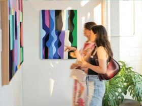 Two women stand admiring a geometric Amy Kim artwork on a gallery wall. A second work hangs behind.