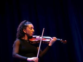 Woman playing violin on stage under blue lighting.