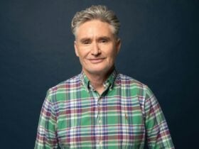 Dave Hughes in a plaid shirt smirking in front of a dark blue wall
