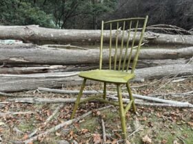 Green democratic chair positioned outside with bark on the ground and timber in the background