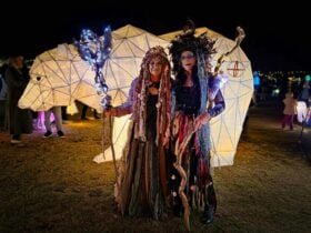 Two people dressed as Sea Hags stand in front of a lantern display at the Lakes Lights event