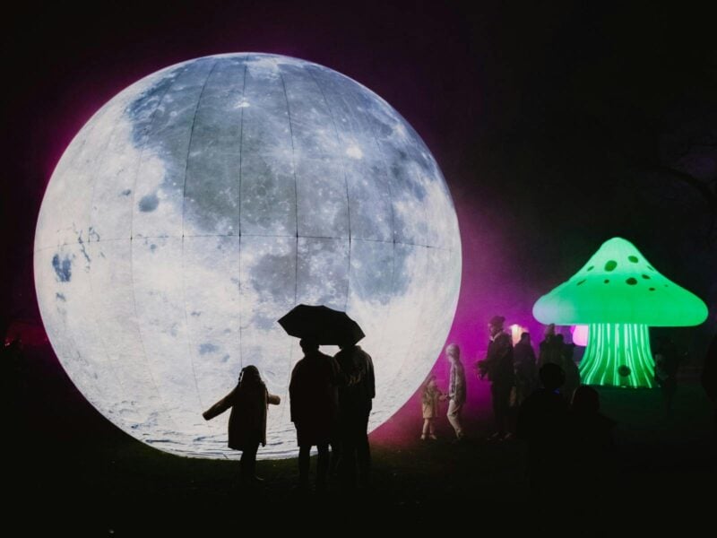 The silhouette of a family standing in front of a ginormous moon installation on the ground.
