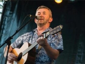 A man holding a guitar singing into a microphone