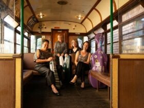 Four female Australian string musicians sitting on a heritage tram and smiling