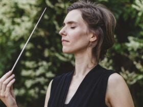 Chloé van Soeterstède standing against a green forest backdrop, baton pointed skyward in her hand