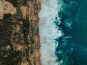 Drone shot of turquoise ocean waves rolling onto a sandy beach beside rocky cliffs.