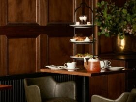 high tea set up on a table with food on high tea trays and cups of tea around it