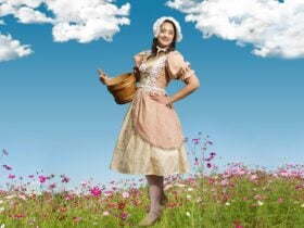 A young white woman with dark hair in a milk maid costume in a flowery meadow