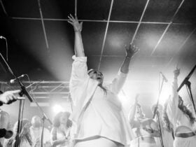 Large group of people on stage singing with hands in air