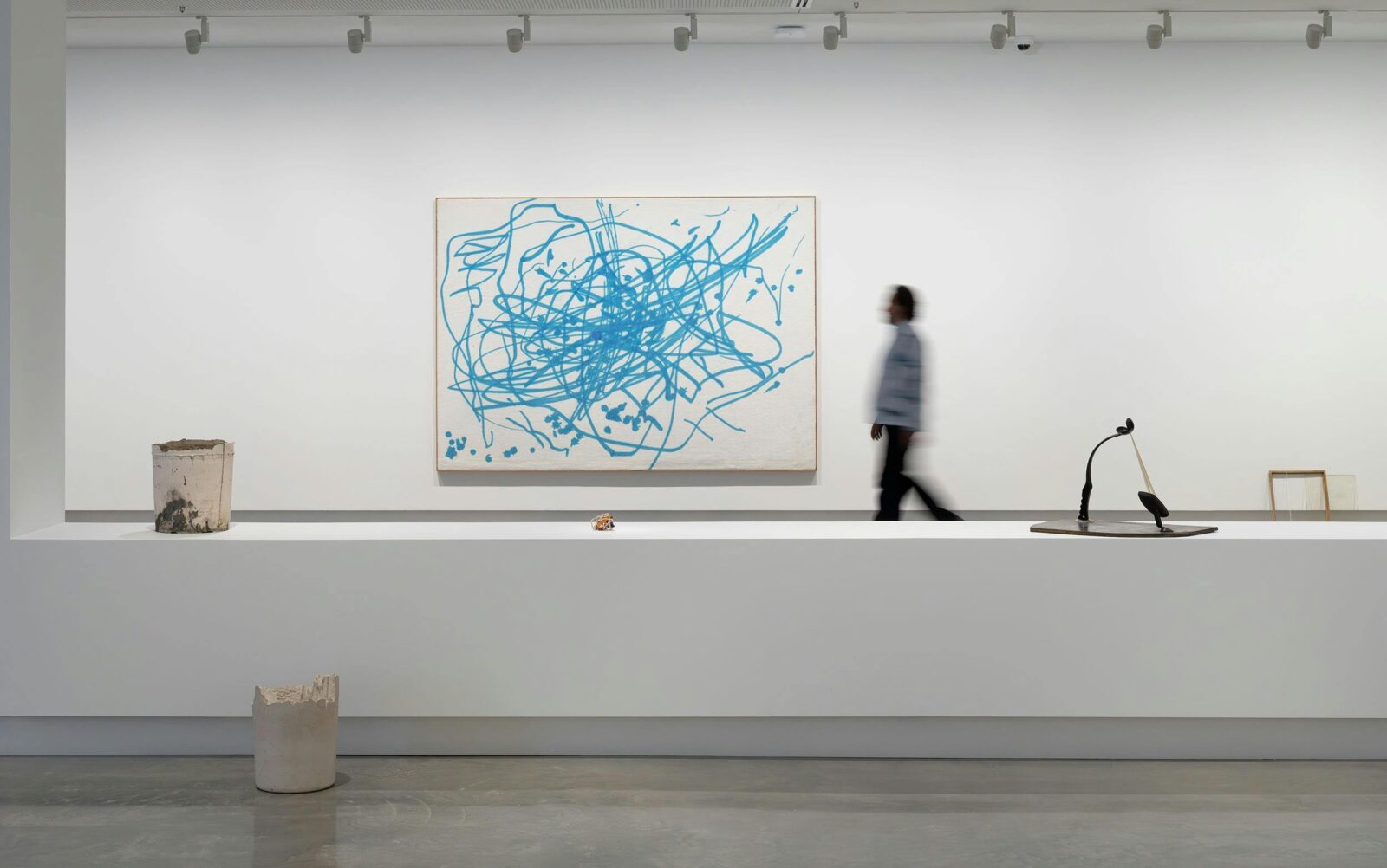 A person walks through a minimalist gallery space with abstract painting on the back wall
