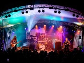 A three-piece band performs on a large lit stage at Blues at Bridgetown festival before a crowd.