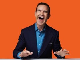 Jimmy Carr laughing in front of orange background