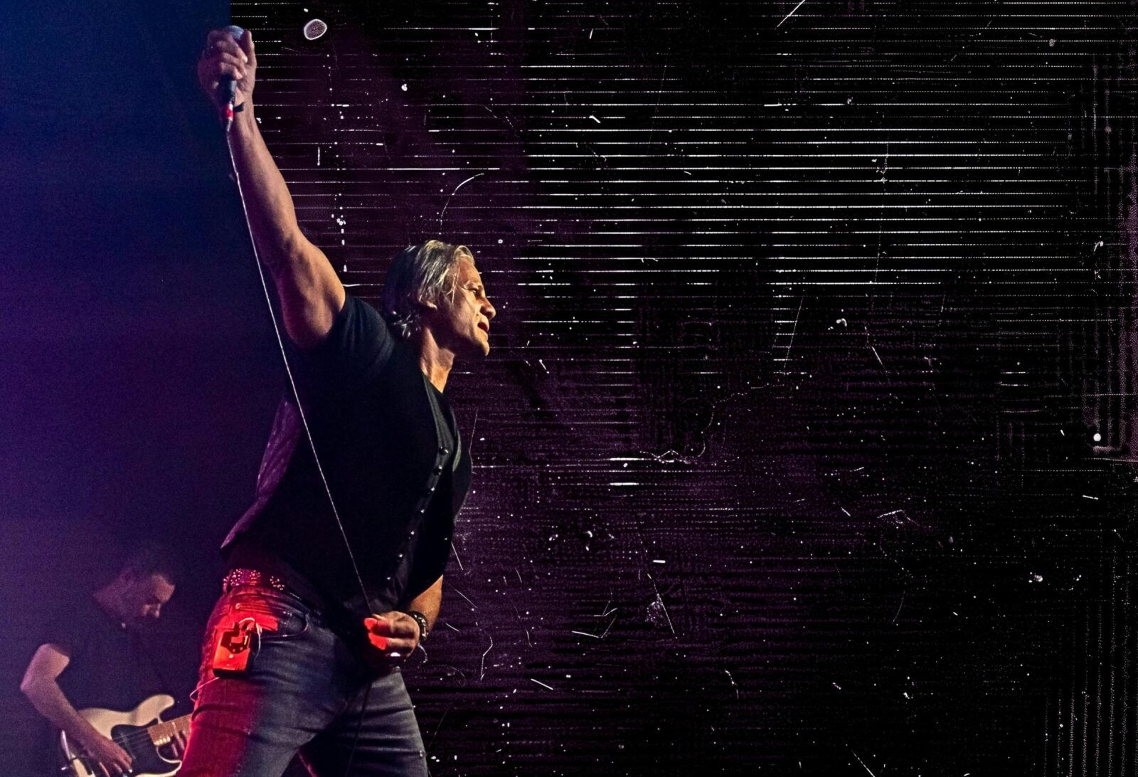 Jon Stevens looking out into the audience with his fist in the air holding a microphone.