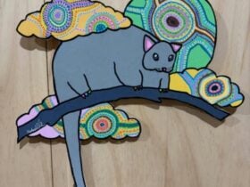 A wood cut brightly painted grey possum surrounded by brightly coloured flora.