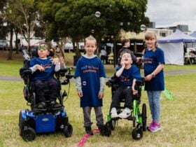 A group of 4 children, 2 wheelchair users, all wearing Ambassadors tees, are smiling