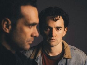 Two men. One looks straight us in crisp focus. The other is in profile, and is out of focus.