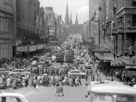 Busy street in a city. People cross the road while trams wait for them.