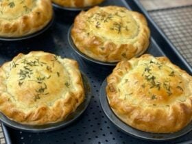 A tray of just cooked indiviual pies, scalloped pastry edge with fresh thyme on top.