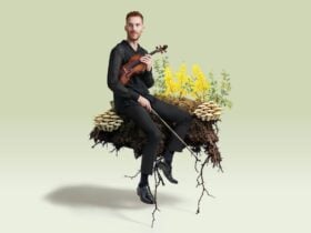 A musician sits on a log with ferns and flowers