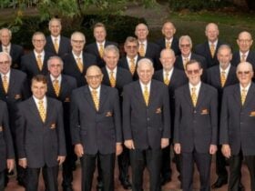 Group of men wearing matching dark suits and yellow ties, standing outdoors for a formal group photo