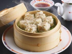 Open steamer basket filled with steamed Sui Mia Dumplings.Background shows dipping sauce and tea.