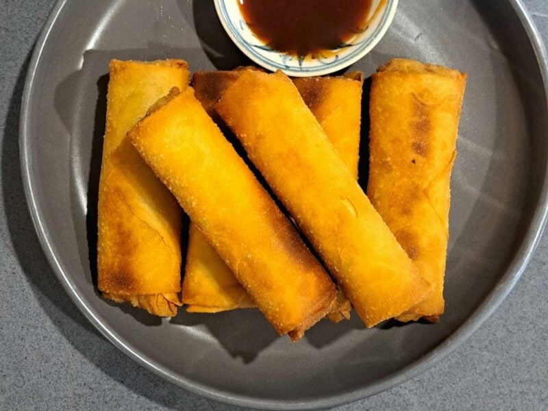 Golden, deep fried spring rolls presented on a platter with dipping sauce.