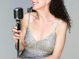 Smiling singer in a silver dress holds a vintage microphone.