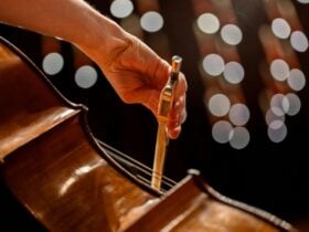 A picture of a hand holding a bow and playing a cello with blurred lights in the background