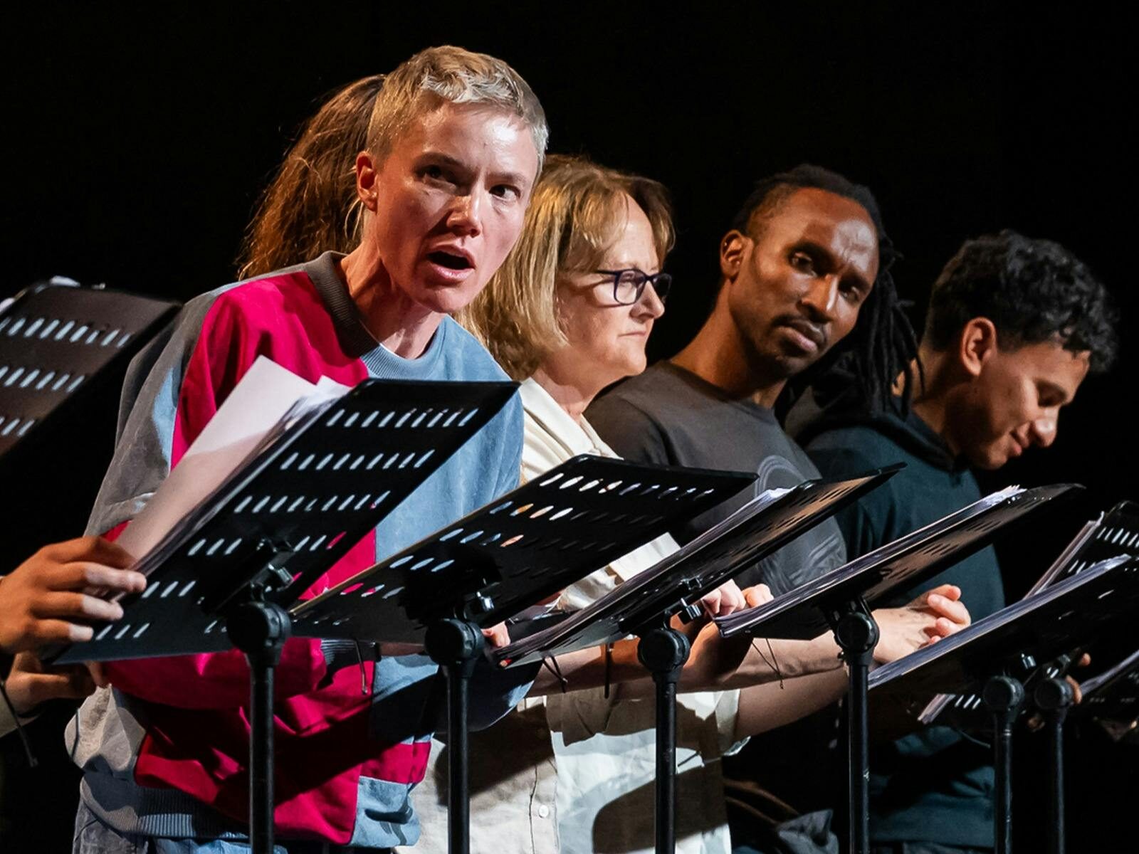 A row of actors standing behind music stands