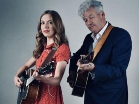 A mand and woman standing side by side holding guitars