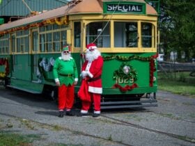 Santa and an elf standing next to a decorated tram