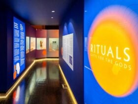 A dark blue hallway entrance to the Rituals exhibition with glowing text panels and glass cabinets